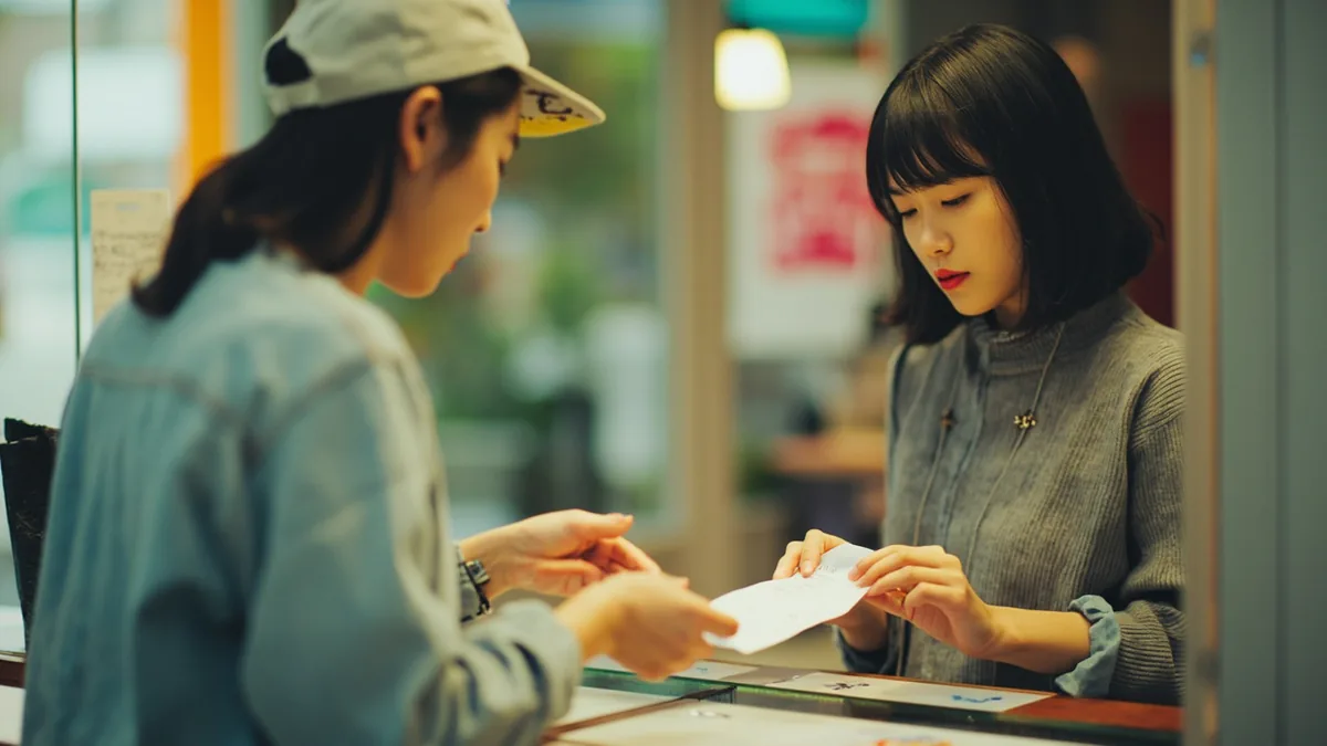 A person hands over money and requests a receipt at a counter, illustrating “a receipt, please” in Chinese: 给我发票 (gěi wǒ fāpiào)