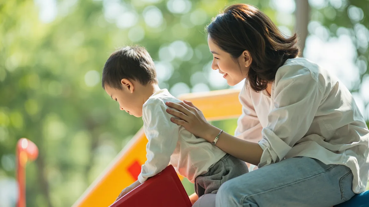 An adult encourages a child to try a small slide at a park, illustrating “be brave” in Chinese: 勇敢一点 (yǒnggǎn yìdian)