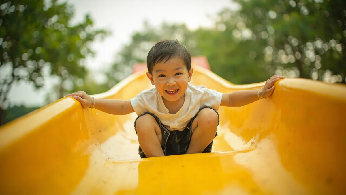 A child slides down a colorful playground slide with joy, illustrating “go down the slide” in Chinese: 滑滑梯 (huáhuáti)