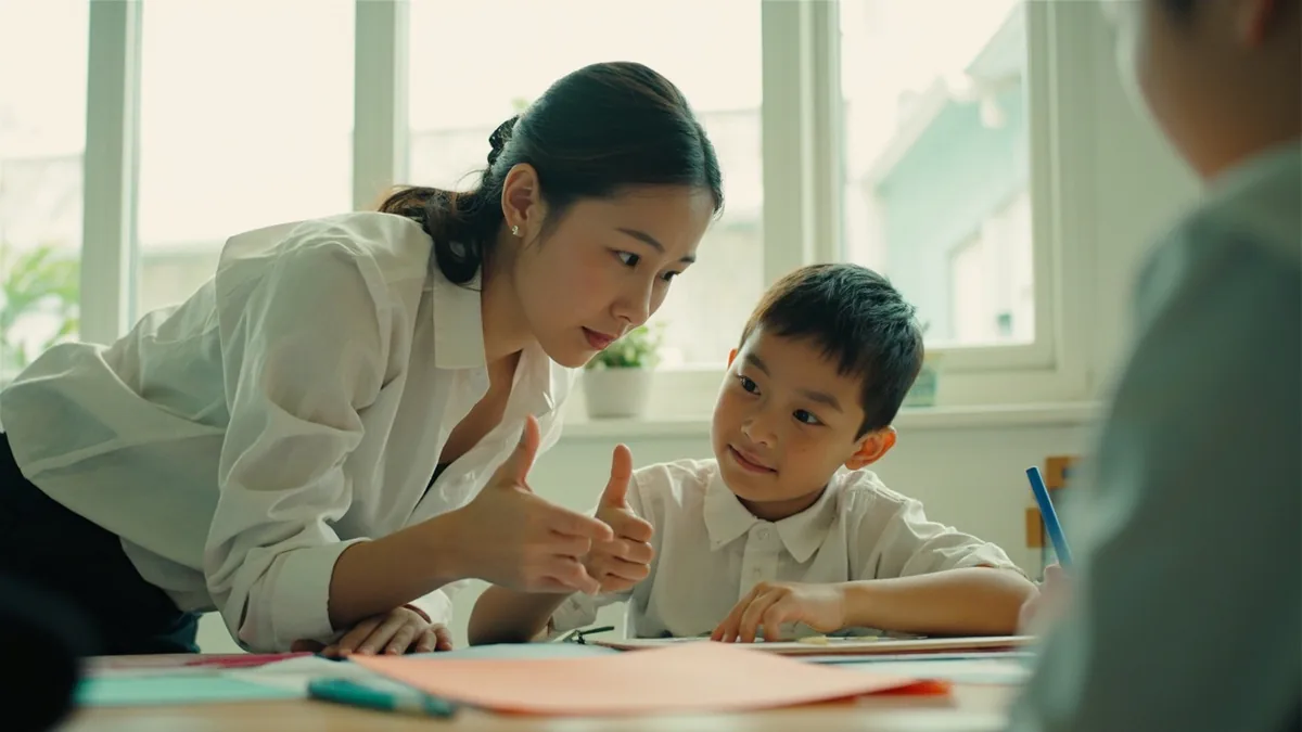 A teacher gives an encouraging thumbs-up to a student's work, illustrating “great job” in Chinese: 真棒！ (zhēn bàng!)