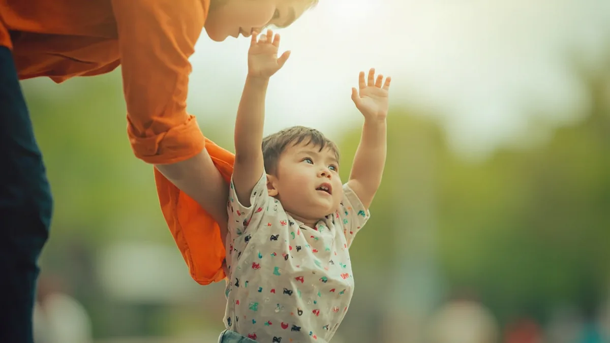 A young child reaches up to their parent asking for a hug, illustrating “hug or carry me” in Chinese: 抱抱 (bàobao)
