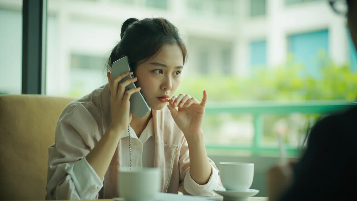 A person gestures apologetically while on a phone call, illustrating “I'll call back later” in Chinese: 我晚点再打 (wǒ wǎndiǎn zài dǎ)