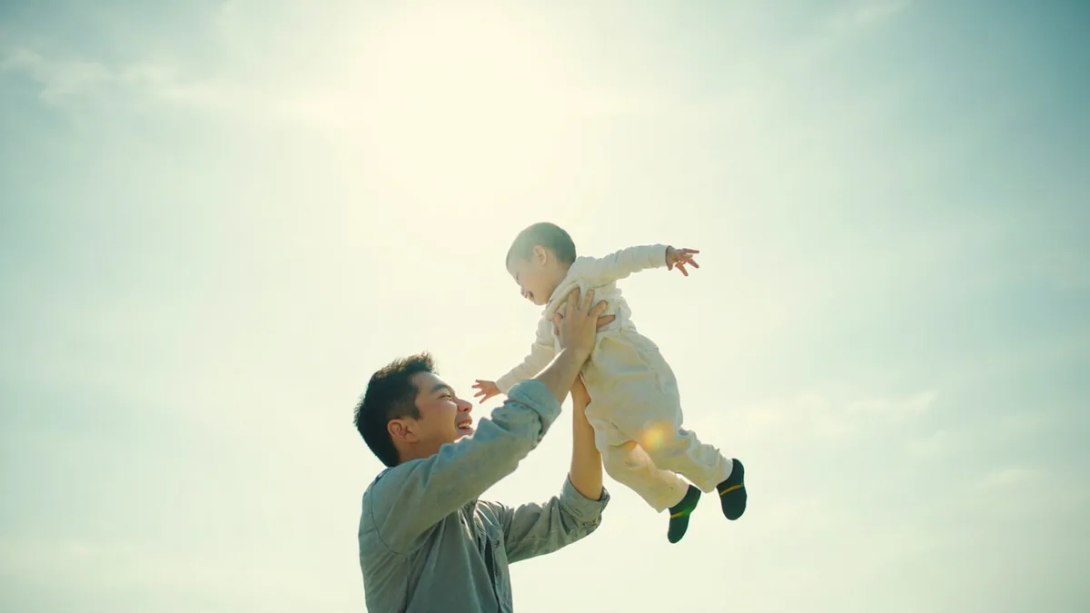 A parent lifts their young child high into the air with playful affection, illustrating “I love you to the moon and back” in Chinese: 我爱你，爱到天涯海角 (wǒ ài nǐ, ài dào tiānyá hǎijiǎo)