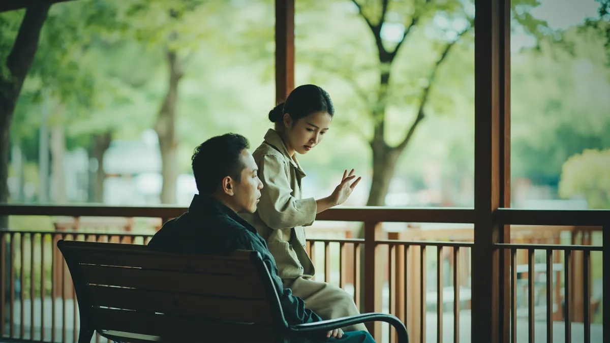 A person gestures toward an empty park bench seat, asking if it is available, illustrating “is this seat taken” in Chinese: 这个座位有人吗？ (zhège zuòwèi yǒurén ma?)