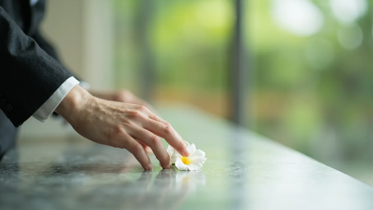 A person places a single white flower at a quiet, respectful memorial site, illustrating “rest in peace” in Chinese: 一路走好 (yílù zǒu hǎo)
