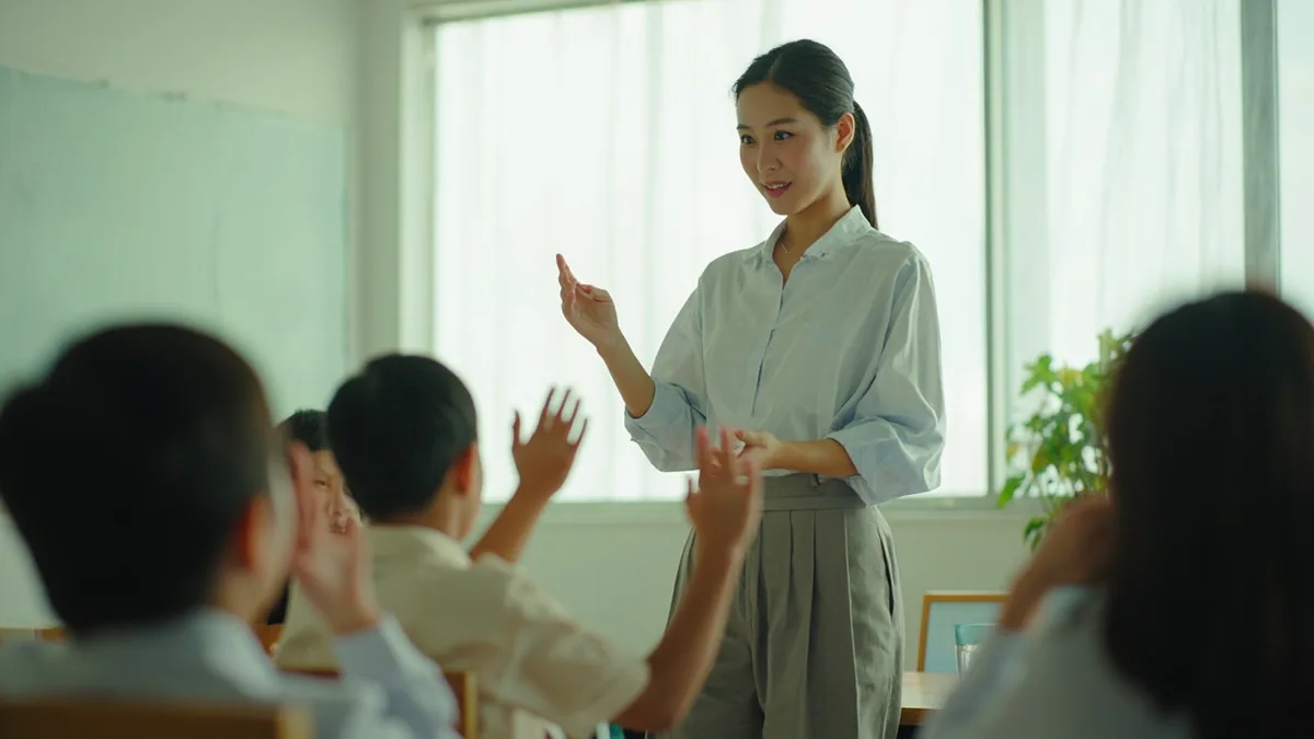 A teacher gestures for students to rise from their seats, illustrating “stand up” in Chinese: 站起来 (zhàn qǐlai)