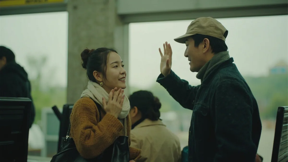 A friend waves goodbye to another at a train station platform, illustrating “take care” in Chinese: 保重 (bǎo zhòng)