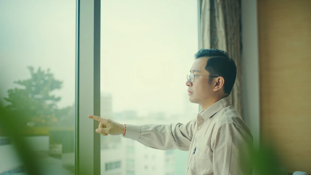 A hotel guest gestures toward a faulty air conditioner unit, illustrating “the air conditioner is broken” in Chinese: 空调坏了 (kōngtiáo huài le)