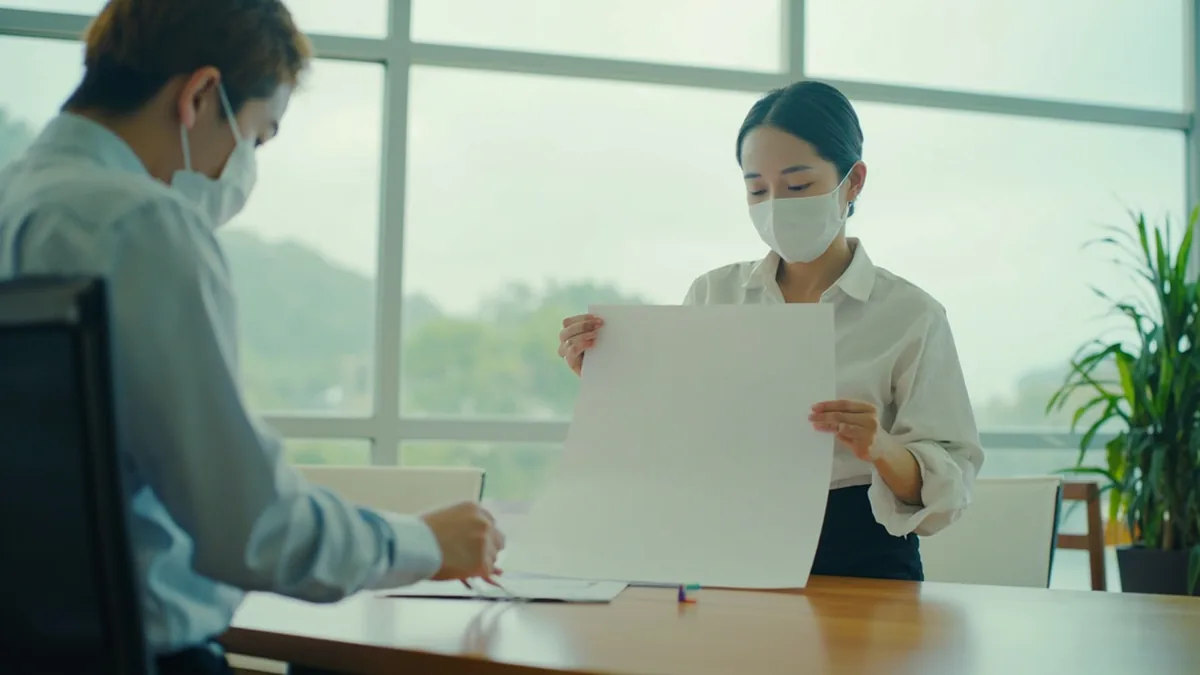 An administrative assistant places a prepared document on a desk, illustrating “the contract is ready” in Chinese: 合同准备好了 (hétong zhǔnbèi hǎole.)