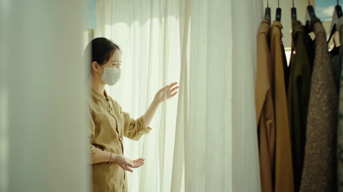A store employee gestures towards a fitting room area, illustrating “the fitting room is over there” in Chinese: 试衣间在那边 (shìyījiān zài nàbian)
