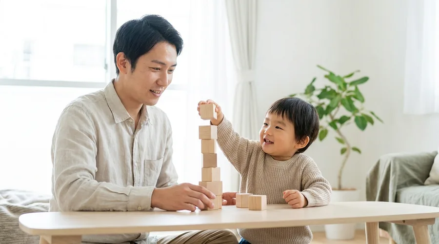 A parent and child stack plain wooden blocks together at a low table